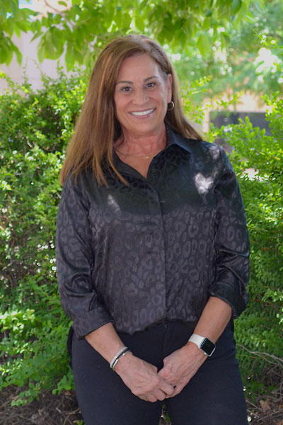 The image features a woman standing outdoors, wearing a black shirt with a leopard print design, smiling slightly, and posing for the photograph.