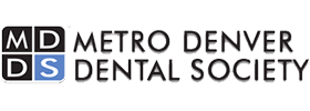 The image displays a logo consisting of text and a graphic element. The text reads 'METRO DENVER DENTAL SOCIETY' with 'METRO DENVER' above 'DENTAL SOCIETY.' Below the main text, there is an emblem featuring a stylized letter 'D' inside a circle. The background of the logo is white, and the text is in black font.