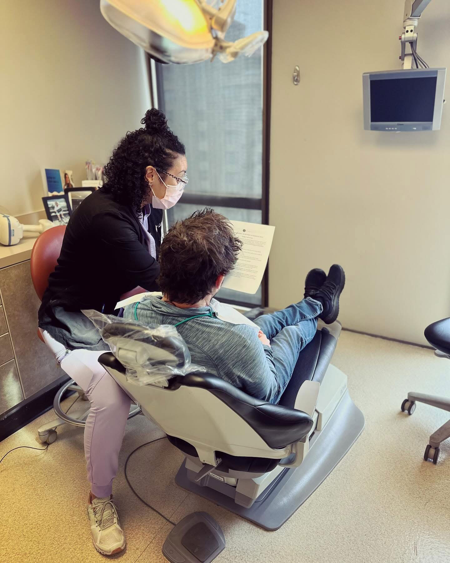 The image shows a dental office setting with a dentist and a patient receiving treatment.