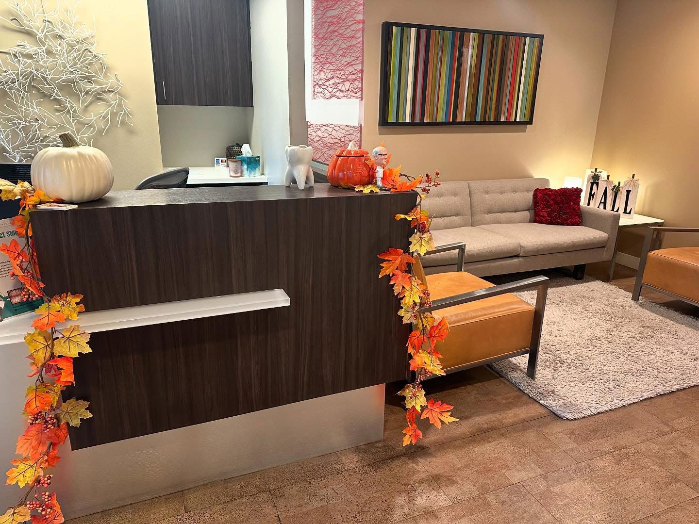 The image shows a reception area with a counter, a sign that reads  Welcome,  a floral arrangement, and decorative fall leaves on a railing.