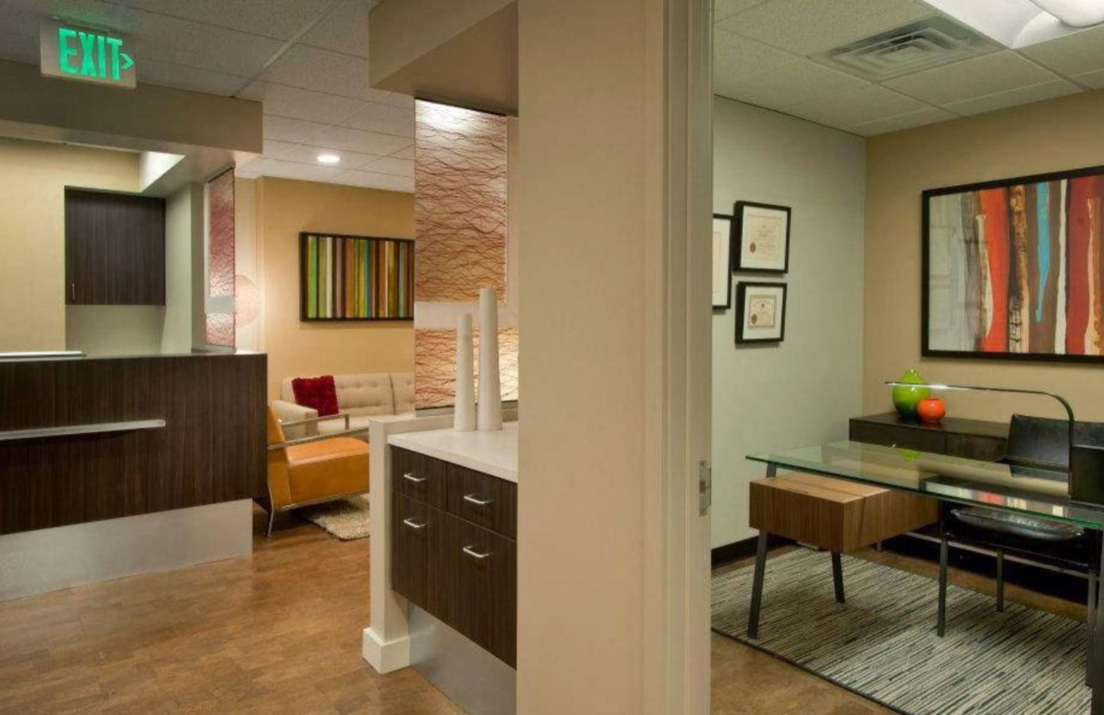 The image shows an interior space that appears to be an office or waiting room with modern furnishings, including a desk, chairs, and a colorful wall decoration.
