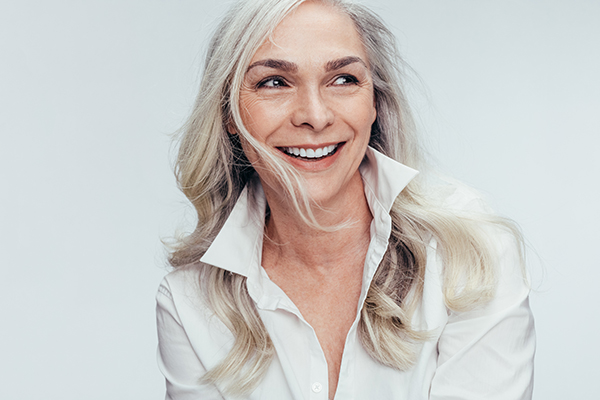 A woman with gray hair smiles at the camera, wearing a white shirt under a dark blazer.