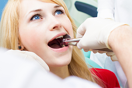 A woman receiving dental care with a dentist using a drill on her teeth.