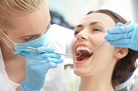 A dental hygienist wearing protective gloves and a mask is performing oral care on a patient s teeth.