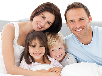 A family of five poses together on a bed, with two adults and three children smiling at the camera.