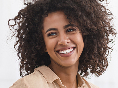 The image shows a smiling person with curly hair, wearing a light-colored top, against a plain background.